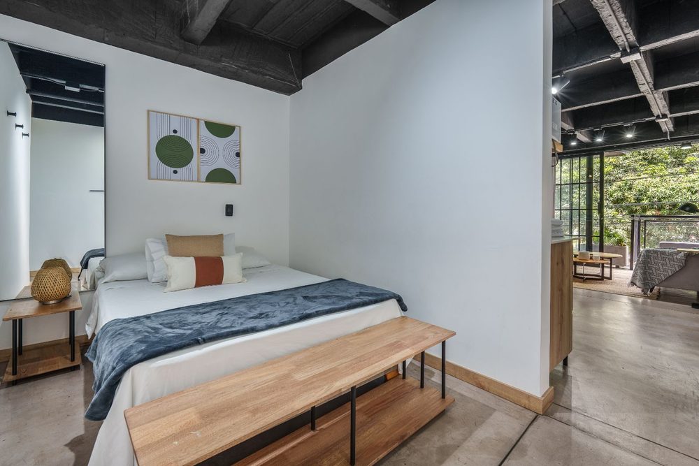 Habitación con cama doble, banca de madera a los pies y salida al balcón