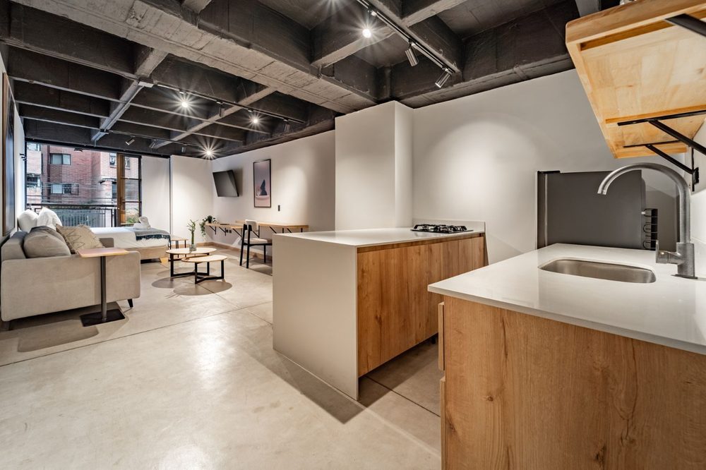 Sala con sofá, comedor junto a la ventana y cocina en madera clara al fondo
